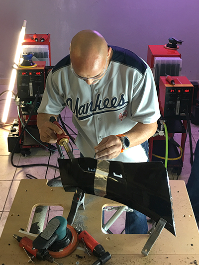 A man using a nitrogen plastic welder to repair part of a bumper.